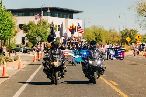 Two police officers on motorcycles lead a parade down a street.