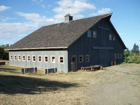 A large grey barn sits in a grassy yard under a partly cloudy sky.