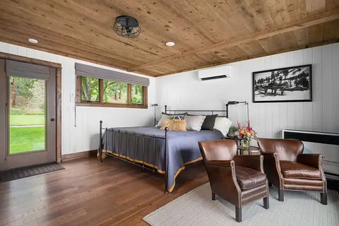 A modern bedroom with a wooden ceiling, metal-frame bed, and two leather armchairs.