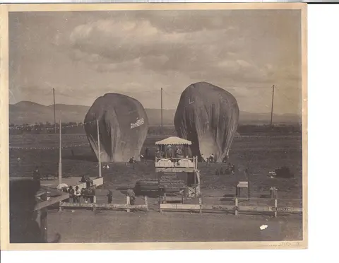 A historic photo shows two large uninflated balloons on a field with people standing nearby.