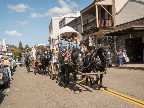 Horse-drawn carriages and riders move down a street lined with historic buildings.
