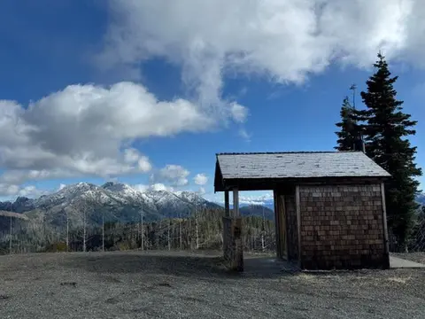 A small wooden building stands on a ridge with snowy mountains visible in the distance.
