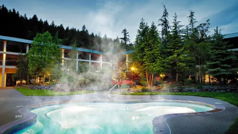 A steaming outdoor hot tub in front of a hotel and forested hill.