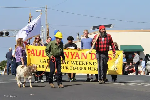 People carrying a yellow banner in a parade on a sunny day.