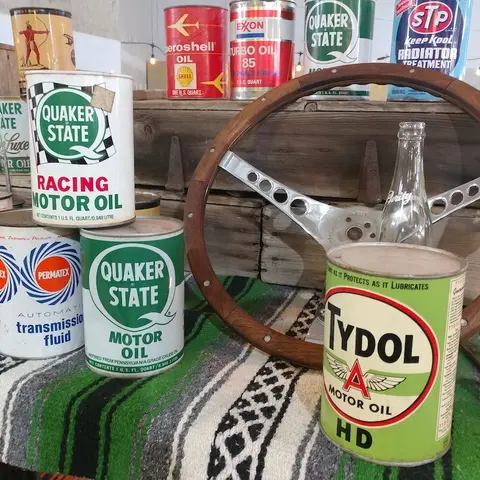 A collection of vintage motor oil cans and a wooden steering wheel displayed indoors.