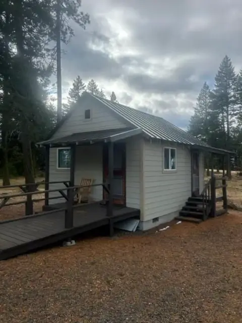 A small cabin with a ramp and porch stands among trees under a cloudy sky.