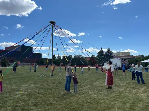People participating in a maypole dance outdoors on a grassy field.