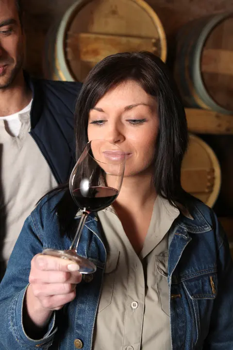 A woman smells a glass of red wine in a cellar.
