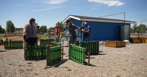 People work outside to set up green and yellow tubes in a gravel yard.