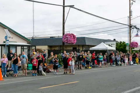 A crowd of people stand along a street, many with their hands over their hearts.