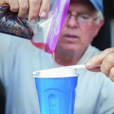 A person pours liquid from a plastic bag through a strainer into a cup.