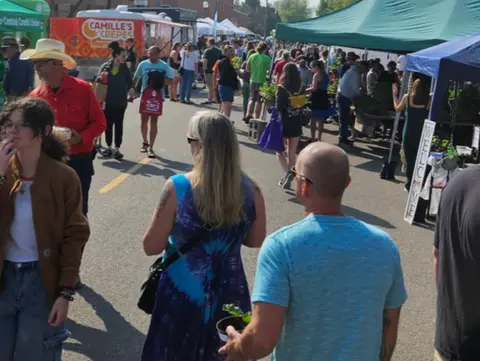 A crowd of people walking through an outdoor market with food trucks and tents.