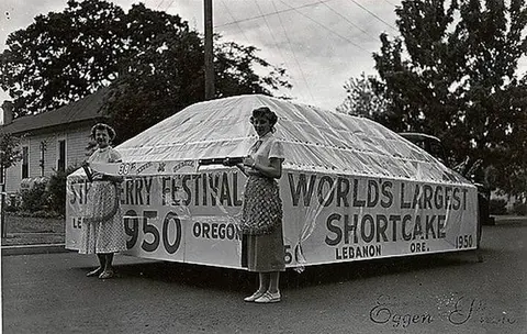 An old photograph showing two women standing next to a large festival float in the street.