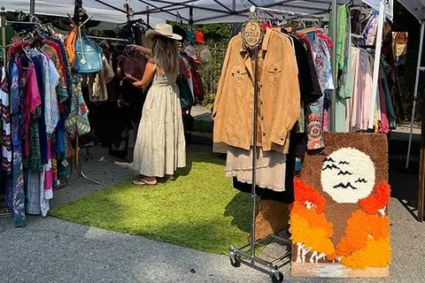 A person browses racks of clothing at an outdoor market stall.