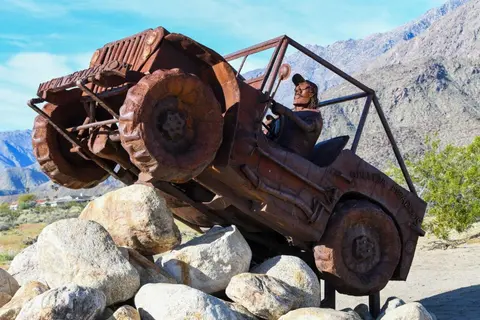 A metal sculpture of a jeep driving over rocks in a desert landscape.