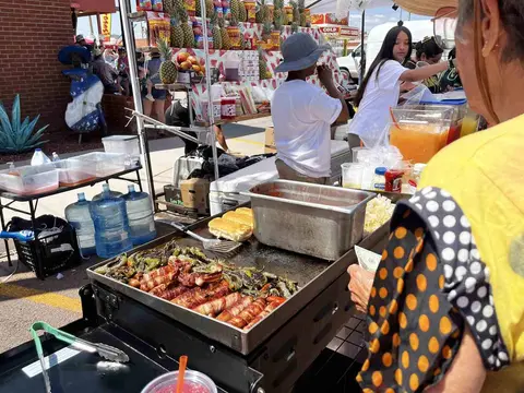 A street vendor cooks bacon-wrapped peppers and serves food and drinks from a stall.