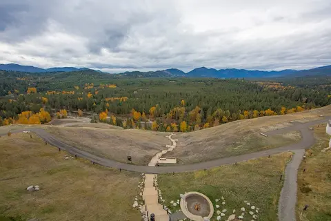 An elevated view of a landscape with rolling hills, walking paths, and distant mountains under a cloudy sky.