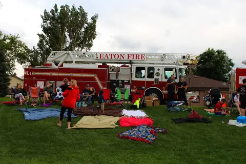 People sitting on blankets and lawn chairs on the grass in front of a fire truck.