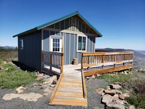 A small cabin with a wooden deck and ramp sits on a mountaintop.