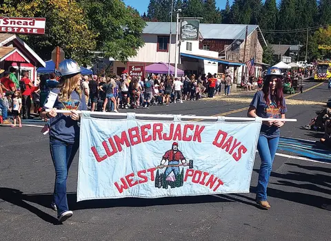 Two people carry a banner reading Lumberjack Days West Point in a parade.