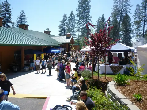 An outdoor market or fair with crowds walking between booths and buildings.