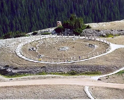 A high-angle view of a large stone circle structure on a mountain ridge.