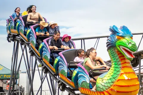People riding a dragon-themed roller coaster at an outdoor event.