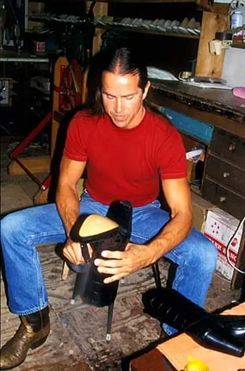 A man sits inside a workshop working on a shoe or boot.