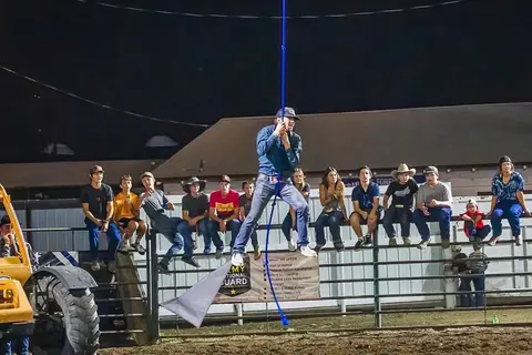 A man swings from a rope at a nighttime event while a crowd watches from a fence.