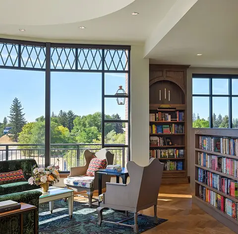A brightly lit library interior with large windows overlooking trees.