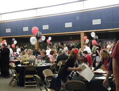 A large group of people gather inside a hall decorated with balloons for an event.