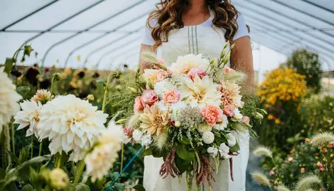 A person holds a large bouquet of flowers inside a greenhouse.