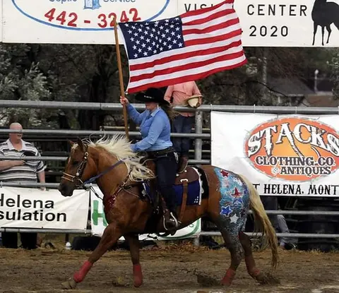 A person on a horse carries an American flag in an arena.
