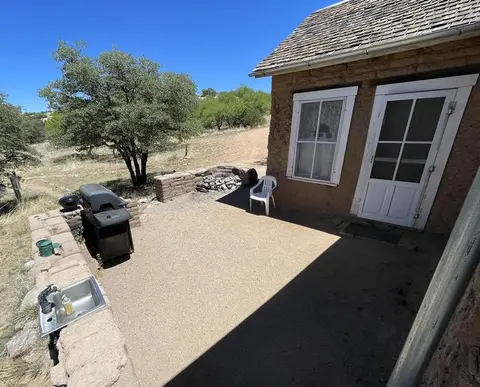 A rustic building exterior with a gravel patio containing a grill, sink, and white chair.