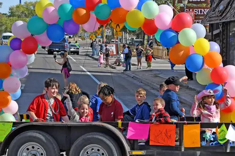 Children riding on a parade float decorated with balloons.