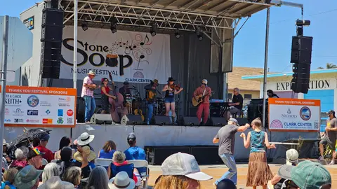 A band performs on an outdoor stage with an audience watching and dancing.