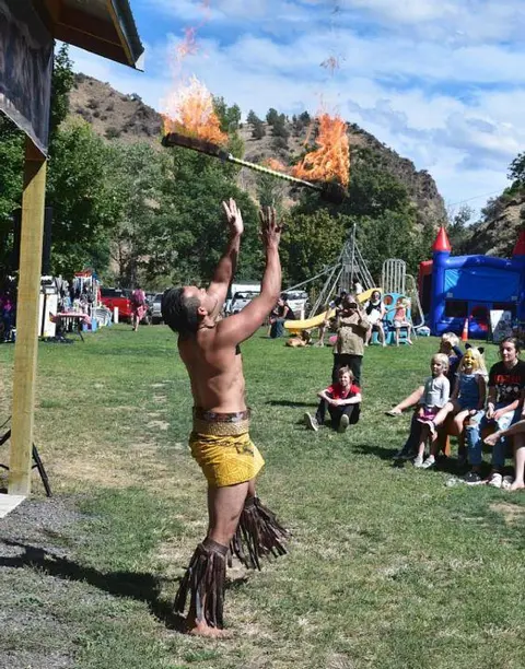 A performer twirls a burning fire staff before an audience outdoors.