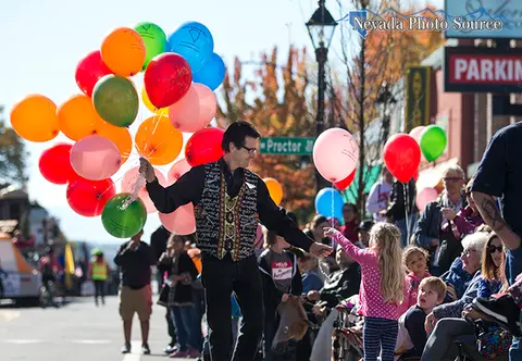A man holding many colorful balloons hands one to a child in a crowd.