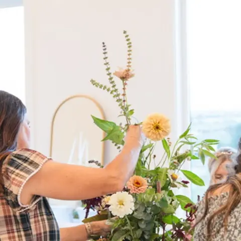 A woman arranges flowers in a bouquet indoors.