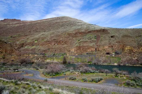 A scenic landscape featuring a river, road, and large hill under a blue sky.