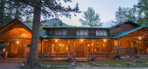 A rustic log cabin exterior illuminated with warm lights at dusk.