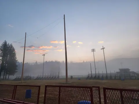 An outdoor sports field at sunrise with fog and tall poles.