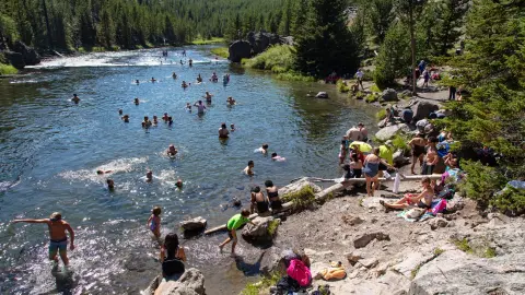 People swimming and relaxing in a river surrounded by trees.