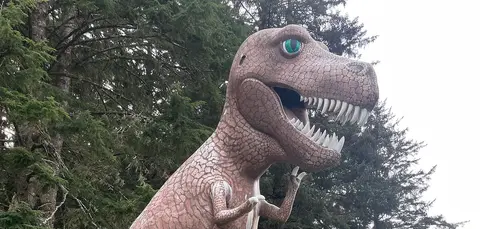 A large dinosaur statue stands among trees.