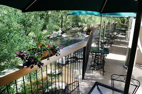 A restaurant patio overlooks a scenic river running alongside lush green trees.