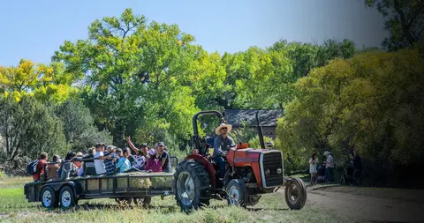 A tractor pulls a trailer carrying a group of people on a farm.