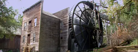 An old wooden mill with a large water wheel turning under a stream of water.