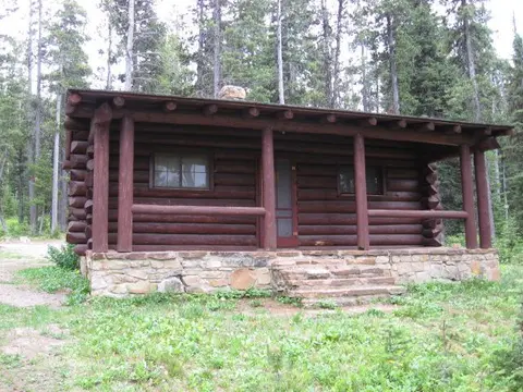 A log cabin sits in a wooded area with a stone foundation.