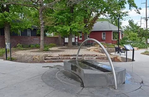 A modern fountain with an arch structure stands in a paved park area.