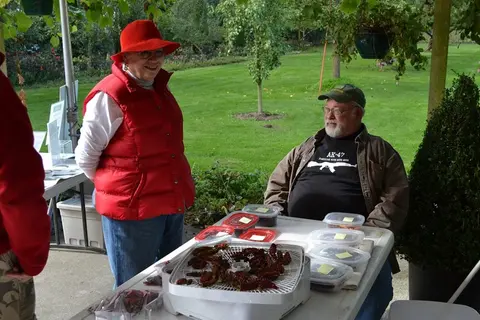 Two people standing and sitting at a table with dried peppers outdoors.